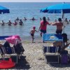 Persone formano un cerchio in mare, ombrelloni blu in spiaggia.