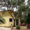 Casa gialla con balcone, circondata da alberi e piante, con area seduta esterna.