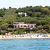 Spiaggia con ombrelloni e sdraio davanti a una casa tra alberi verdi.