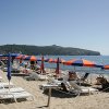 Spiaggia sabbiosa con lettini bianchi e ombrelloni blu e arancioni, vista su collina.