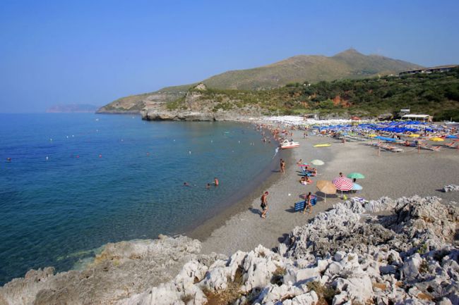 Spiaggia con ombrelloni colorati, mare calmo e montagne sullo sfondo.