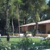 Un'area verde con erba e fiori davanti a un edificio con tetto in tegole e portico, alberi intorno.